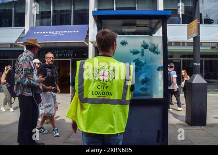 Un operaio ispeziona la scatola di sentinelle della polizia nella City di Londra con la nuova opera d'arte di Banksy che raffigura una scuola di pesci. Questa è la settima nuova opera d'arte a tema animale in sette giorni nella capitale dall'elusivo artista di strada. (Foto di Vuk Valcic / SOPA Images/Sipa USA) Foto Stock