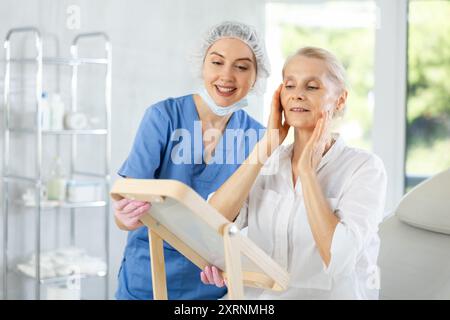 Paziente anziana soddisfatta che tiene lo specchio seduto sulla sedia clinica Foto Stock