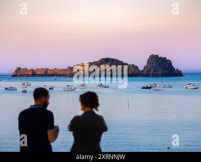 Cancale, Francia - 19 luglio 2024: Sereno tramonto costiero in Bretagna con figure sagomate, barche e aspro sfondo dell'isola. Foto Stock