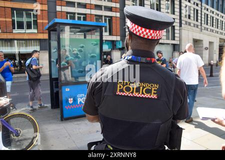 Londra, Regno Unito. 11 agosto 2024. Un agente di polizia osserva le persone che si riuniscono intorno alla scatola di sentinelle della polizia con la nuova opera d'arte di Banksy nella City di Londra. L'opera d'arte, raffigurante una scuola di piranha, è la settima nuova opera d'arte in altrettanti giorni a Londra dell'inafferrabile artista di strada. Crediti: Vuk Valcic/Alamy Live News Foto Stock