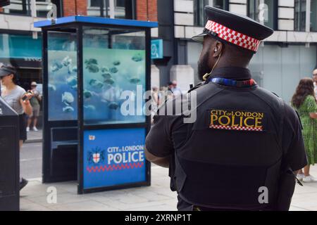 Londra, Regno Unito. 11 agosto 2024. Un agente di polizia osserva le persone che si riuniscono intorno alla scatola di sentinelle della polizia con la nuova opera d'arte di Banksy nella City di Londra. L'opera d'arte, raffigurante una scuola di piranha, è la settima nuova opera d'arte in altrettanti giorni a Londra dell'inafferrabile artista di strada. Crediti: Vuk Valcic/Alamy Live News Foto Stock