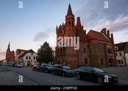 9 agosto 2024, Sassonia-Anhalt, Tangermünde: Il municipio sulla piazza del mercato la sera con il muro di mattoni alto 24 metri. Chiesa di Santo Stefano sullo sfondo a sinistra. Foto: Jens Kalaene/dpa Foto Stock