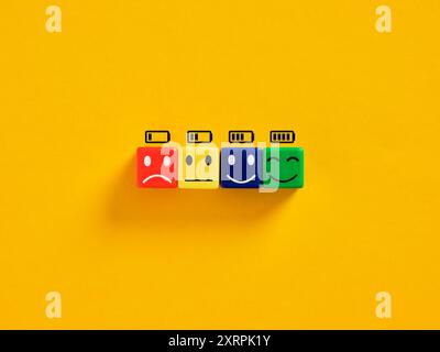 Livello della batteria e ricarica. Felicità, vitalità e benessere mentale. Quattro cubi colorati mostrano livelli di carica della batteria diversi con emoji corrispondenti Foto Stock