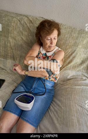 Donna anziana che misura la pressione sanguigna a casa. Ispanico donna anziana che misura la pressione sanguigna utilizzando il monitor digitale per la salute e il benessere Foto Stock