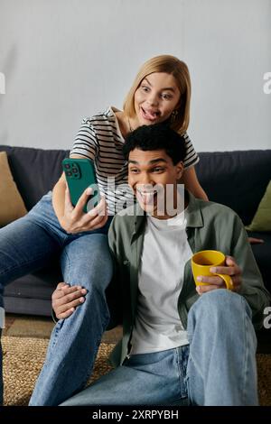 Una giovane coppia multiculturale fa un selfie insieme mentre fa facce divertenti nel loro appartamento moderno. Foto Stock