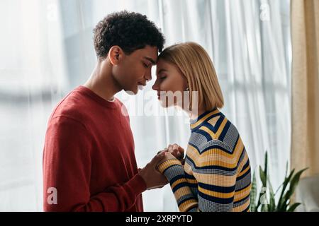 Una felice coppia multiculturale si trova nel loro appartamento, con la fronte che si tocca mentre condividono un momento tenero. Foto Stock