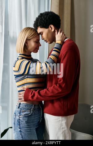 Una coppia variegata abbraccia un appartamento moderno, mostrando affetto con la fronte toccata. Foto Stock