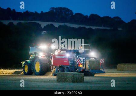 Gli agricoltori lavorano fino a tarda notte raccogliendo il raccolto all'inizio di agosto. Gli agricoltori utilizzano potenti luci sui loro trattori in modo da poter raccogliere fino a tarda sera. La fattoria si trova nella campagna del Warwickshire, nelle Midlands, nel Regno Unito. Foto Stock