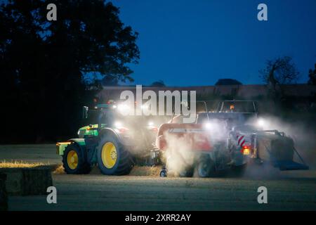 Gli agricoltori lavorano fino a tarda notte raccogliendo il raccolto all'inizio di agosto. Gli agricoltori utilizzano potenti luci sui loro trattori in modo da poter raccogliere fino a tarda sera. La fattoria si trova nella campagna del Warwickshire, nelle Midlands, nel Regno Unito. Foto Stock