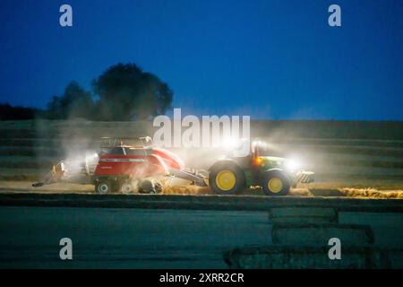 Gli agricoltori lavorano fino a tarda notte raccogliendo il raccolto all'inizio di agosto. Gli agricoltori utilizzano potenti luci sui loro trattori in modo da poter raccogliere fino a tarda sera. La fattoria si trova nella campagna del Warwickshire, nelle Midlands, nel Regno Unito. Foto Stock