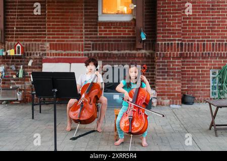 Vista superiore di due bambini seduti sul patio a giocare al violoncello Foto Stock