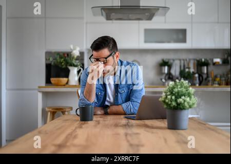 Uomo d'affari stanco e ansioso con la testa in mano seduta accanto al computer portatile alla scrivania in ufficio Foto Stock