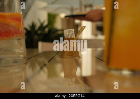 Un piccolo vaso d'oro con un pezzo di carta dentro. Il vaso si trova su un tavolo con un bicchiere di succo d'arancia e una pianta in vaso Foto Stock