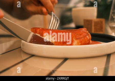 Una persona sta tagliando un pezzo di torta con un coltello e una forchetta. Il cibo è su un piatto bianco per dessert. La scena è informale e rilassata, con la persona Foto Stock