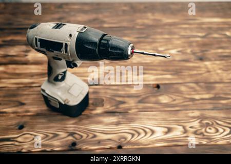 Su un tavolo di legno è presente un trapano a batteria. Uno strumento di lavoro. Concetto fai da te Foto Stock