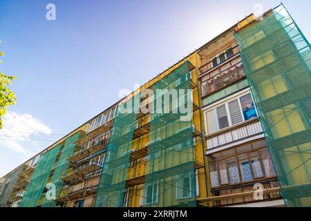 Un edificio di appartamenti giallo con impalcature e rete verde Foto Stock