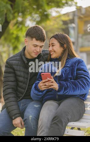 Ragazza latina e ragazzo caucasico innamorato seduto su una panchina in un parco pubblico. Foto Stock