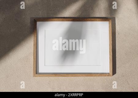 Mockup con cornice orizzontale in legno vuoto. Poster appeso. Ombre di foglie di palma sulle pareti calcaree beige alla luce del sole. Sfondo naturale astratto Foto Stock