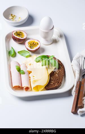 Prosciutto, formaggio, pane e uova sode sul piatto della colazione, sfondo bianco. Foto Stock