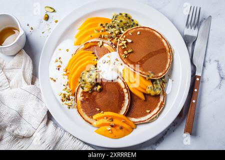 Pancake con mango e frutta della passione su un piatto bianco, vista dall'alto. Ricetta vegana sana. Foto Stock