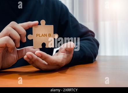 Testo 'PLAN B'on puzzle pezzo tenuto per mano di un uomo d'affari, su un tavolo di legno con spazio per le copie. Obiettivo aziendale e successo, proc. Di leadership Foto Stock