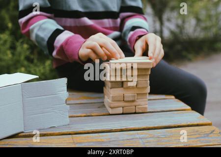 Persona che impilava blocchi di legno, costruiva la torre mentre era seduto a un tavolo all'aperto, concentrandosi sul bilanciamento dei pezzi. Primo piano Foto Stock