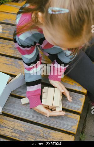 Persona che impilava blocchi di legno, costruiva la torre mentre era seduto a un tavolo all'aperto, concentrandosi sul bilanciamento dei pezzi. Primo piano Foto Stock