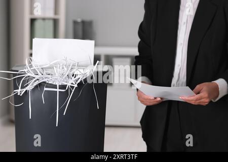 Donna che distrugge fogli di carta con trituratore in ufficio, primo piano Foto Stock