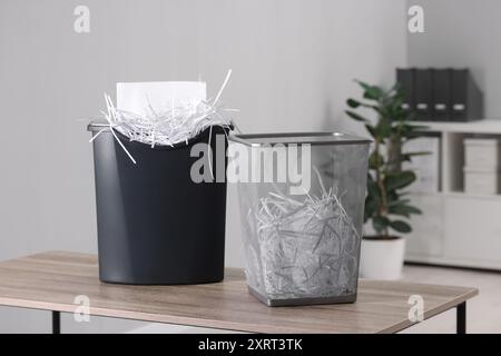 Distruggendo fogli con trituratore e strisce di carta in un cestino di metallo su un tavolo di legno in ufficio Foto Stock