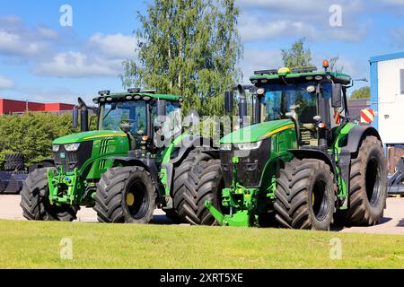 Trattori agricoli John Deere 6215R e John Deere 7310R parcheggiati su un terreno asfaltato. Salo, Finlandia. 22 giugno 2024. Foto Stock