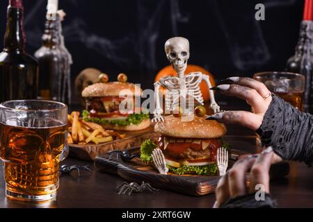 Le mani delle streghe vogliono prendere il Monster Burger sullo scheletro seduto. Perfetto antipasto per la festa di Halloween Foto Stock