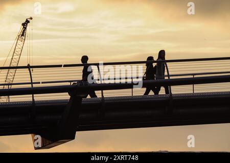 Persone che camminano sul ponte al tramonto con Crane sullo sfondo Foto Stock