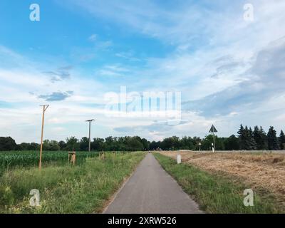 Una strada con una mediana erbosa e qualche albero sullo sfondo. Il cielo è blu con alcune nuvole Foto Stock