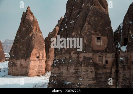 Camini delle fate ricoperti di neve in Cappadocia, Turchia, con antiche abitazioni scavate nelle formazioni rocciose uniche Foto Stock