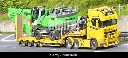 Appaltatori Scania e Yellow con semi-rimorchio a pala bassa carica nuova macchina per movimentazione materiali Sennebogen 835E tedesca che guida l'autostrada M25 Essex Inghilterra Regno Unito Foto Stock