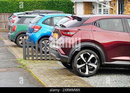 Linea di colori assortiti su auto a motore berlina parcheggiate in spazi anteriori con giardino all'esterno di case private strada residenziale Essex Inghilterra Regno Unito Foto Stock