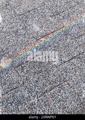 Un arcobaleno si riflette su un tetto grigio. Il tetto è fatto di piastrelle e presenta alcune crepe Foto Stock