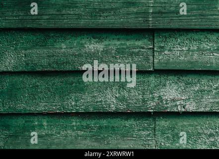 Una parete di legno verde con molta vernice sbucciante. Il muro è composto da diverse tavole di legno e la vernice si sta frammentando in alcuni punti. La scena lo è Foto Stock