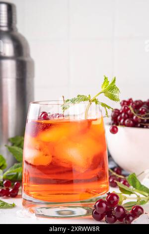 Caipirinha al ribes rosso, limonata o sangria con cubetti di ghiaccio e succo di lime, su un tavolo da cucina bianco spazio copia Foto Stock