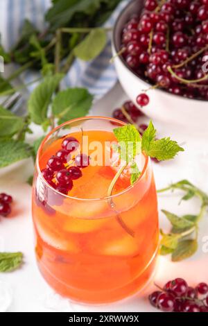 Caipirinha al ribes rosso, limonata o sangria con cubetti di ghiaccio e succo di lime, su un tavolo da cucina bianco spazio copia Foto Stock