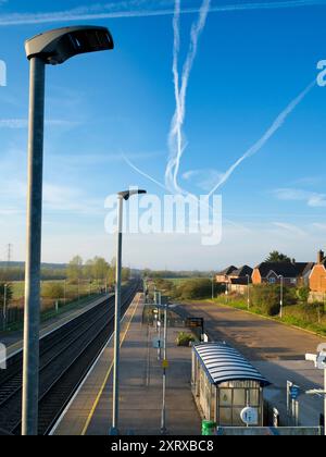 Radley è fortunato ad essere un piccolo villaggio con una stazione ferroviaria principale, che lo collega a Londra, Oxford e le Midlands. E qui, visto dal ponte della stazione sui binari, vediamo una linea di lampioni e una serie di telecamere di sicurezza che si affacciano sulla piattaforma. Il cielo primaverile è pieno di contrafforti che si estendono in blu. Foto Stock