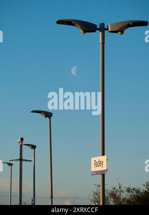 Radley è fortunato ad essere un piccolo villaggio con una stazione ferroviaria principale, che lo collega a Londra, Oxford e le Midlands. E qui vediamo una linea di lampioni che si affacciano sulla piattaforma, con una luna primaverile che guarda in basso. Foto Stock