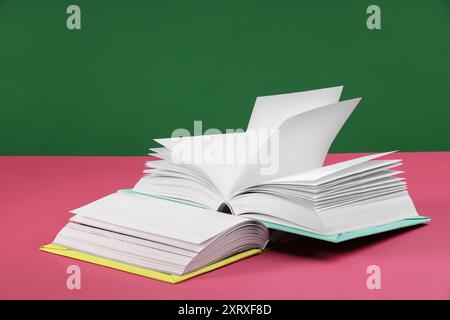 Libri colorati su tavolo rosa su sfondo verde Foto Stock