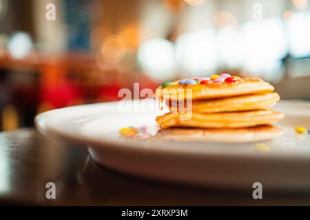 Goccia di miele che gocciola una pila di pancake con lenticchie al cioccolato colorate Foto Stock