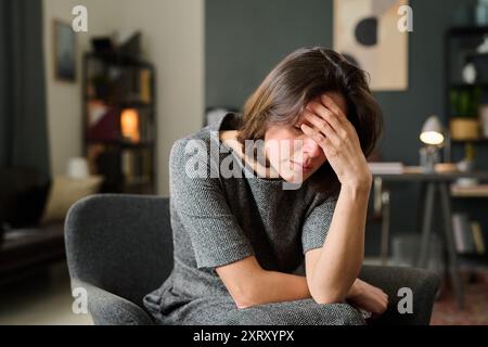 Donna seduta sulla sedia che tiene la testa in mano Foto Stock