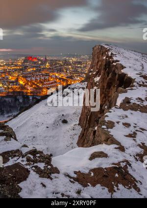 Vista verticale di Edimburgo, Scozia, coperta di neve dall'Arthur Seat al crepuscolo, con luci stradali che illuminano la città Foto Stock