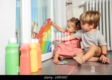 I bambini seduti al chiuso dipingono un arcobaleno vibrante sulla finestra Foto Stock