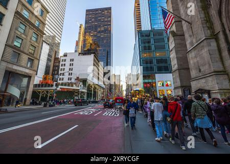 5th Avenue a Manhattan, New York, piena di auto e pedoni che camminano sui marciapiedi tra grattacieli torreggianti. Nuovo Yor. STATI UNITI. Foto Stock