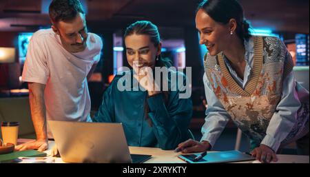 Energici compagni di squadra che fanno brainstorming per la strategia di marketing in un ufficio creativo di notte. Gruppo multietnico di persone che lavorano allo sviluppo di idee di crescita basate sui dati utilizzando un computer portatile Foto Stock