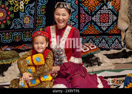 Donna e bambino nomadi in abito tradizionale all'interno di una yurta decorata ad Almaty, Kazakistan Foto Stock